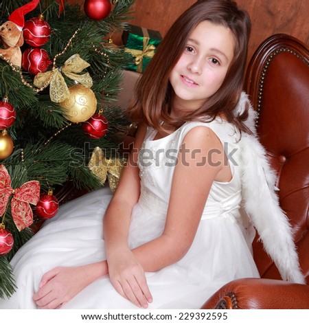 Lovely portrait of little Angel with Christmas gifts over Christmas tree full of beautiful decoration on Holidy theme/Lovely angel with white wings on Holiday theme