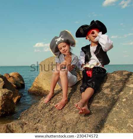 Beautiful young kids pirate boy and girl holding a pirate map and a magnifying glass looking for buried treasure on the beach