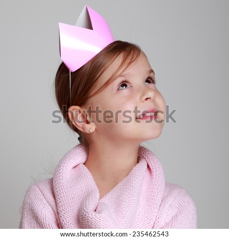 Studio portrait of a beautiful Caucasian girl with a charming smile in a knitted dress with a pink crown holding a gift on a gray background/Beauty little princess with pink tiara