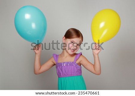 Beautiful little girl with a sweet smile, holding a yellow and blue air balloon on Holiday
