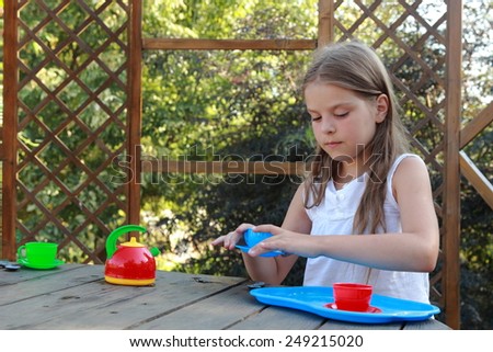 Happy little girl playing with children\'s dishes in the tea party outdoor