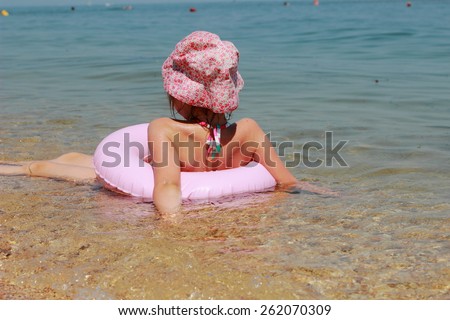 Cute little girl in panama swims in the sea with clean water with a lifeline in a sunny summer day