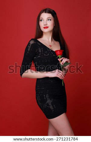 Charming young woman in a black dress holding a single red rose on a red background