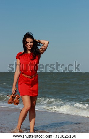 Beautiful woman walks at the sea side. Wet, red dress, high heels shoes.