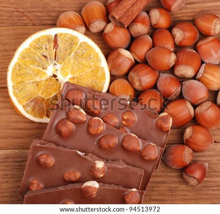bars milk chocolate with hazelnuts and slice of dry orange, lots of hazelnuts and a stick of cinnamon as a background on a food and drink concept theme/chocolate with hazelnuts