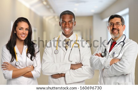Group of three diverse doctors with arms crossed inside hospital building
