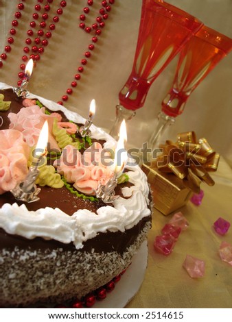 celebratory table (birthday cake and candles, two red glasses with champagne, gift box) on golden