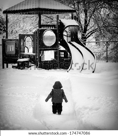 Small child looks longingly at the local playground which is dangerously covered in snow and ice. Wishing it was spring when it will be again safe to play on it.   Dramatic Black and White processed.