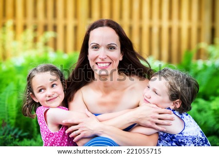 A close up family picture of two daughters on either side of their mother giving her a hug.