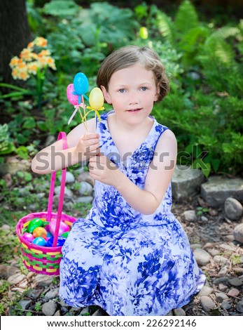 A portrait of a happy young girl sitting outside smiling holding an Easter basket and Easter eggs during an Easter egg hunt.