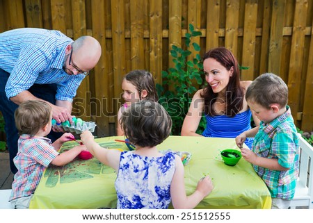Family painting and decorating eggs outside during the spring season in a garden setting.  Mother and father with children together color dyeing Easter eggs.  Part of a series.