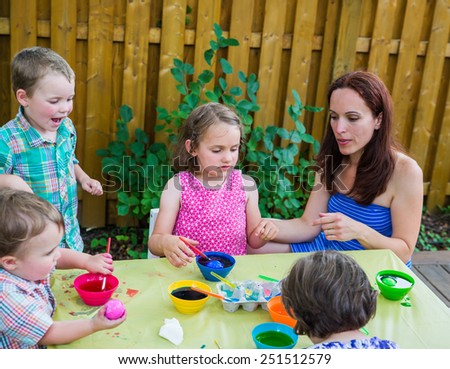 Family of children painting and decorating eggs outside.  Mother and kids have fun as they paint their color dyed Easter eggs during the spring season in a beautiful garden setting.  Part of a series.