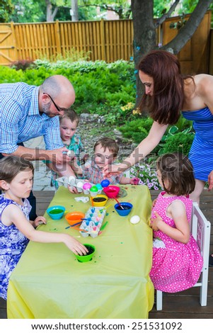 Family with children painting and decorating eggs together during the spring season in a outdoor garden setting.  Mother and father help the kids color dye their Easter eggs.  Part of a series.