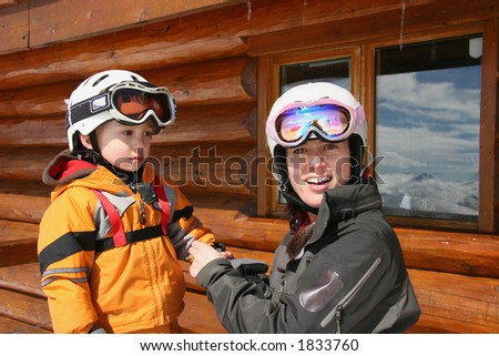 Mother and toddler wearing helmets take a break at a log cabin hut on a beautiful spring ski day.