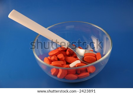 A bowl and spoon with a serving of red pills with one odd white one sit on a blue background.