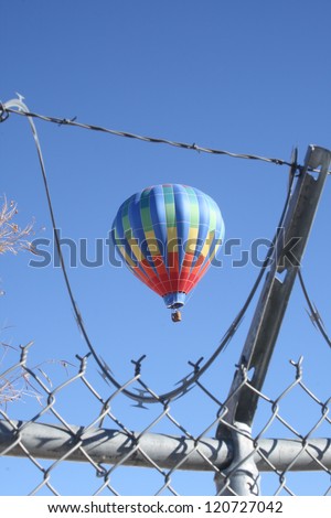 A hot air balloon in the Albuquerque Balloon Festival, seen through a barbed wire and chain link fence, showing they are prevented from landing and limiting freedom of flight - vertical orientation