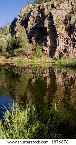 A stone cliff face rises above a calm pond, reflected in the water.