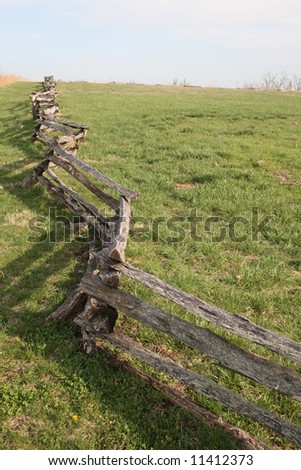 A split-rail fence runs up a hill in a green field in the springtime