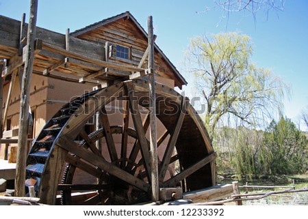 A old, but fully-working water-driven mill, with a rather large wooden waterwheel, located on the grounds of a museum in New Mexico, complete with adobe walls