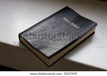 Bible on white shelf in natural light, with shallow depth of field, focused on \