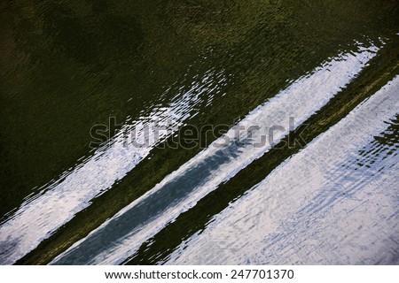 Light reflections on water, a kind of abstract. The water surface is quite calm and dark greenish and the light forms some kind of stripes over it with some white and a little blue reflections