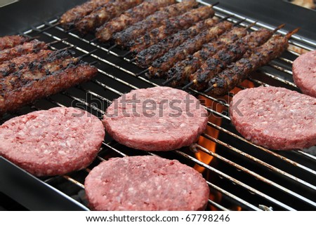 Lamb skewers and beef burgers cooking on a garden outdoor barbecue over hot charcoal.
