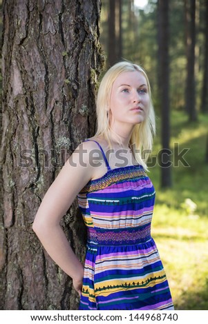 Zoomed woman in lined dress rests on tree