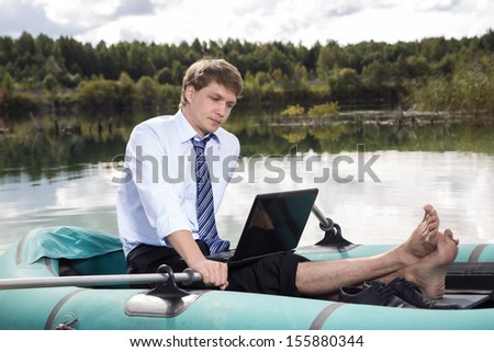 Dressed man in boat and reading from laptop
