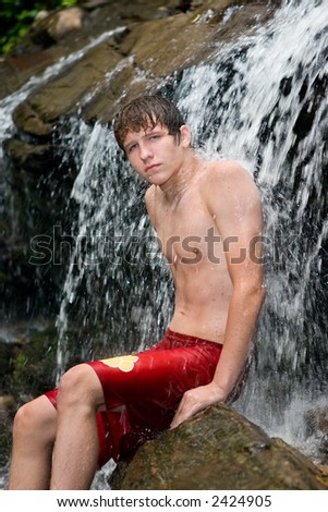 Teenage boy sitting in waterfall with the water flow rolling over his chest and off his back.