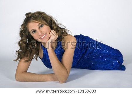 Three-quarters front view of classy and sophisticated looking teen brunette model up on her elbows while lying down on white seamless background.