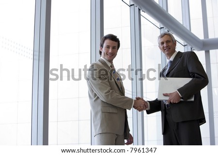Two businessmen shaking hands in front of large glass widows