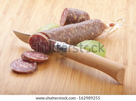 Pieces of smoked sausage with green basil and knife on the wood