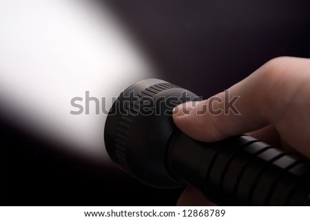 Close up of man\'s hand holding black  torch, with beam of light visible.