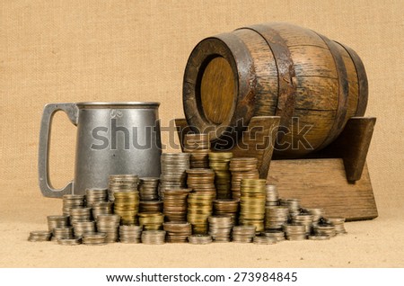 Stack of coins with aluminum mug and wooden barrel on brown sack background