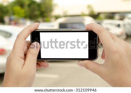 Smart phone in woman\'s hand on blur car park background with clipping path