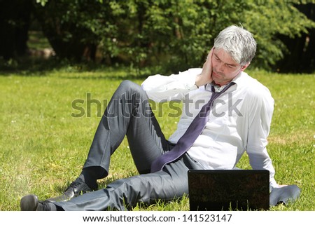 A young handsome businessman using laptop on a meadow. Worried about the final outcome./Worried businessman using laptop on a meadow