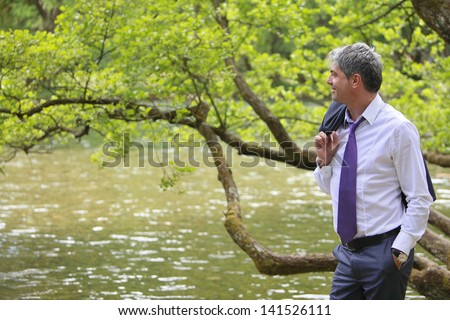 A young self-confident businessman standing in the nature, near a river and looking to the distance.../My success are my efforts