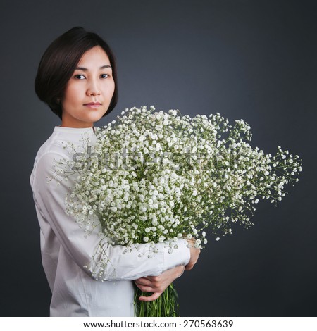 Young asian woman in a white shirt with a big bouquet of white flowers in hands on dark background