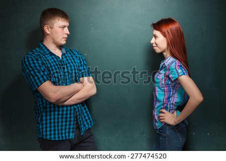 Young couple, man and woman make a claim to each other looking in eyes each other. Collision of interests in relationships. Red-haired woman and blonde man in check shirts.