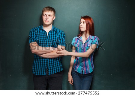 Portrait Of Beautiful Young Couple Over Dark Green Wall. Hard times in relationships. Woman apologizes. Reconciliation. Red-haired woman and blonde man in check shirts.