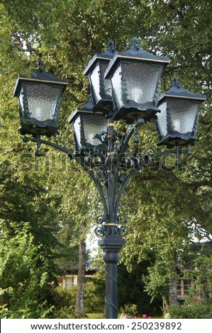 A street lantern with five individual lamps, in the background  trees/Forging work