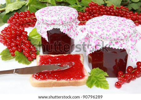 Two glasses of homemade red currant jam with fresh fruits, leaves and a toast