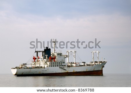 Image shows a white merchant ship floating over calm waters