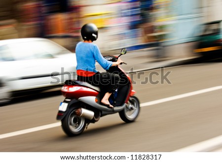 Panning shot of a young girl riding a scooter in a European city