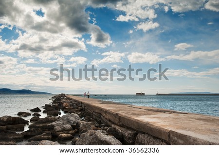 A couple in the distance strolling along the pier in Kalamata, southern Greece, under a spectacular cloudscape