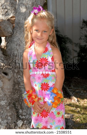 A beautiful little girl dressed in a tropical print dress with a flower in her hair.