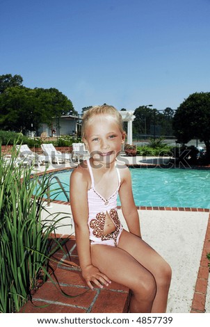 Cute little girl sitting on  a brick wall outdoors by the pool.