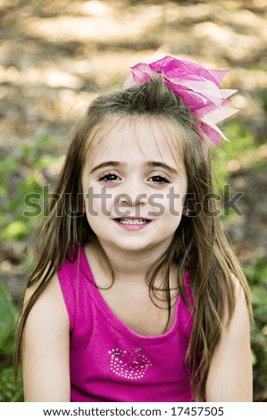Beautiful little girl with a big pink bow in her hair.  She has a beautiful smile with perfect baby teeth.