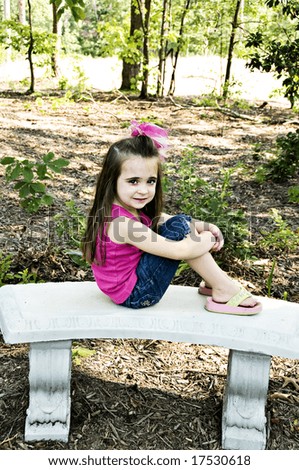 A beautiful little girl dressed in pink sitting on a concrete garden bench.  She\'s wearing flip-flops and has a sweet expression on her face.