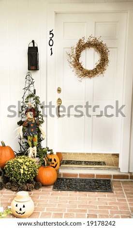 A Fall door adorned with a wreath and surrounded by pumpkins, pinecones and jack-o-laterns.